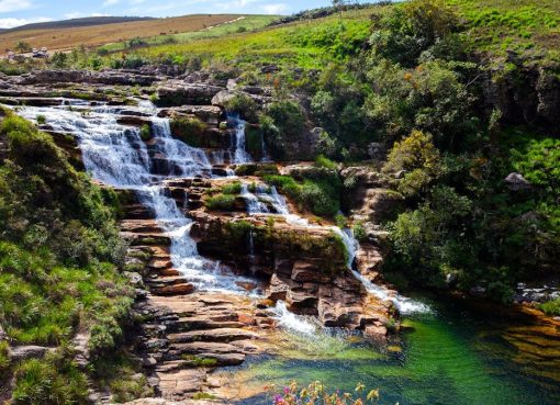 A vibrant and serene waterfall cascading through lush greenery with a clear pool below, set amidst a vast natural landscape.
