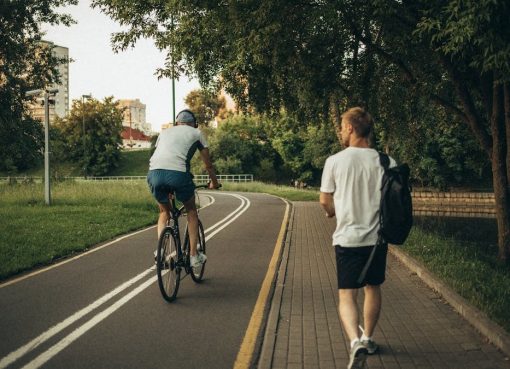 A cyclist and a walker enjoy a peaceful park trail surrounded by greenery.
