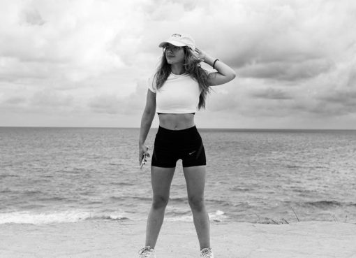 A woman in athletic attire poses near the ocean with a dramatic sky in Natal, Brazil.